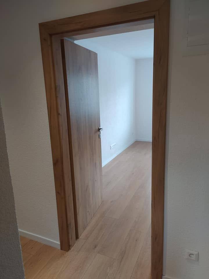 Offene Tür in dunklerem Eichendekor, die in ein helles, leeres Zimmer führt.