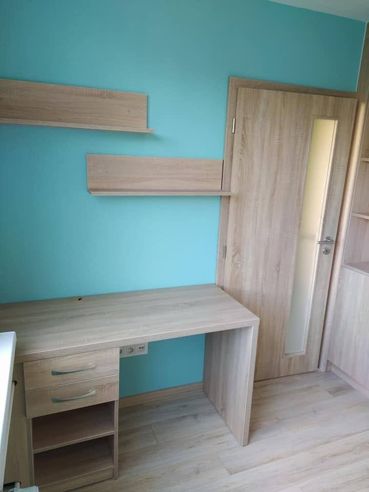 Schreibtisch mit Container und zwei Borden an türkiser Wand