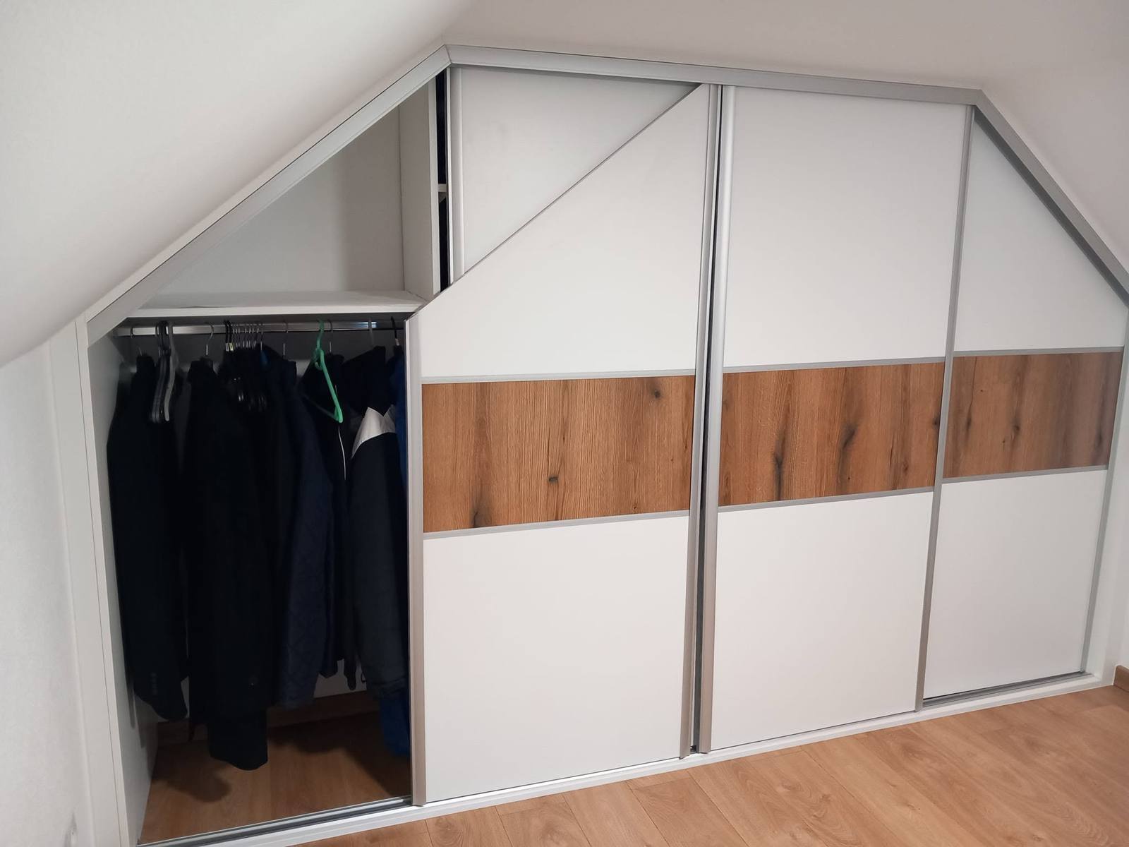 Geöffnete äußere Tür des Dachschrägenkastens mit Kleidung auf der Stange