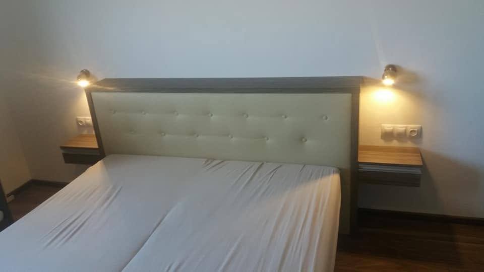 Bett mit gestepptem Kopfteil, hängenden Nachtkästchen und Wandleuchten