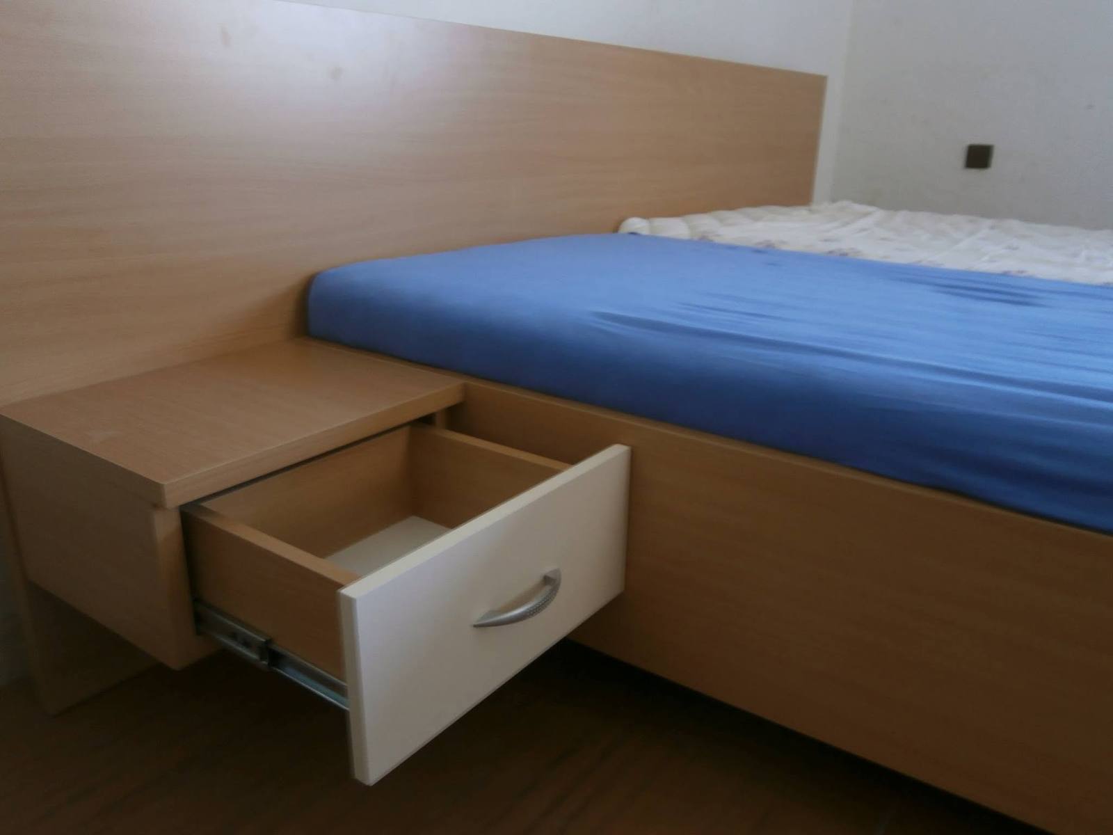 Posteľ s vysokým čelom a nočným stolíkom s otvorenou zásuvkou