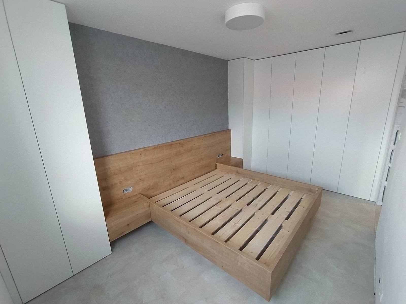 Bett in Eichendekor mit Wandpaneel zwischen weißen Einbaukästen