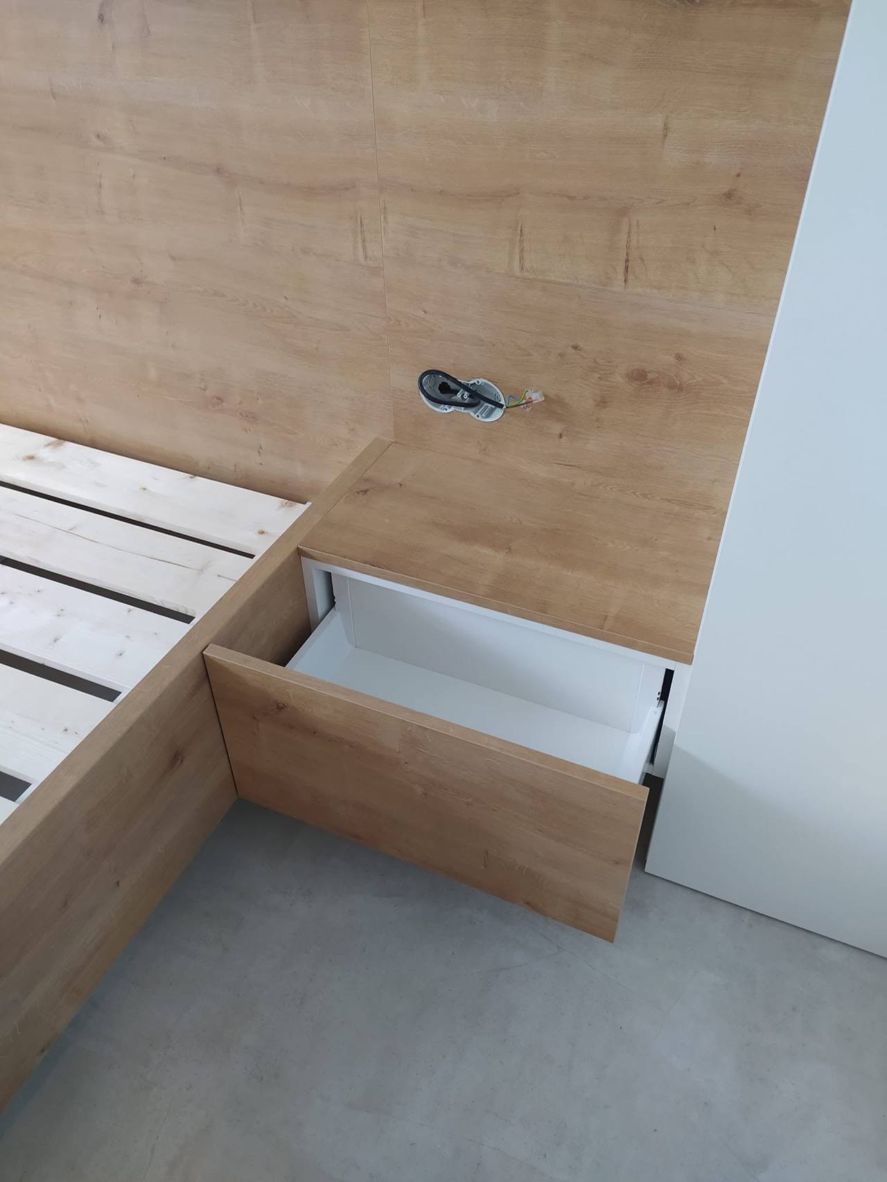 Geöffnete Lade unter dem Nachtkästchen und Steckdose im Paneel