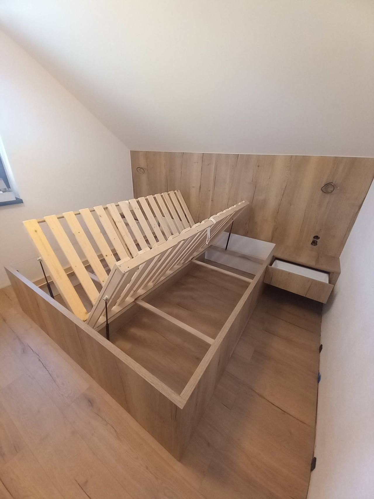 Geöffneter Stauraum des Bettes in Eichendekor unter der Schräge