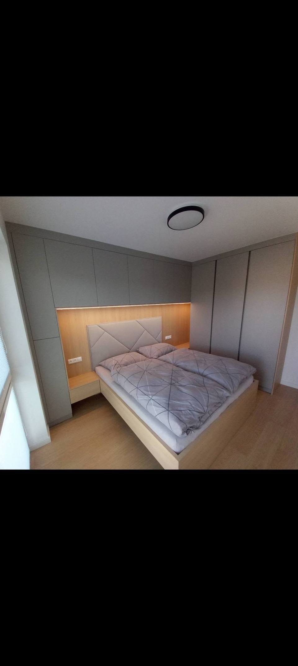 Bett unter grauen Oberkästen und neben hohem Kasten