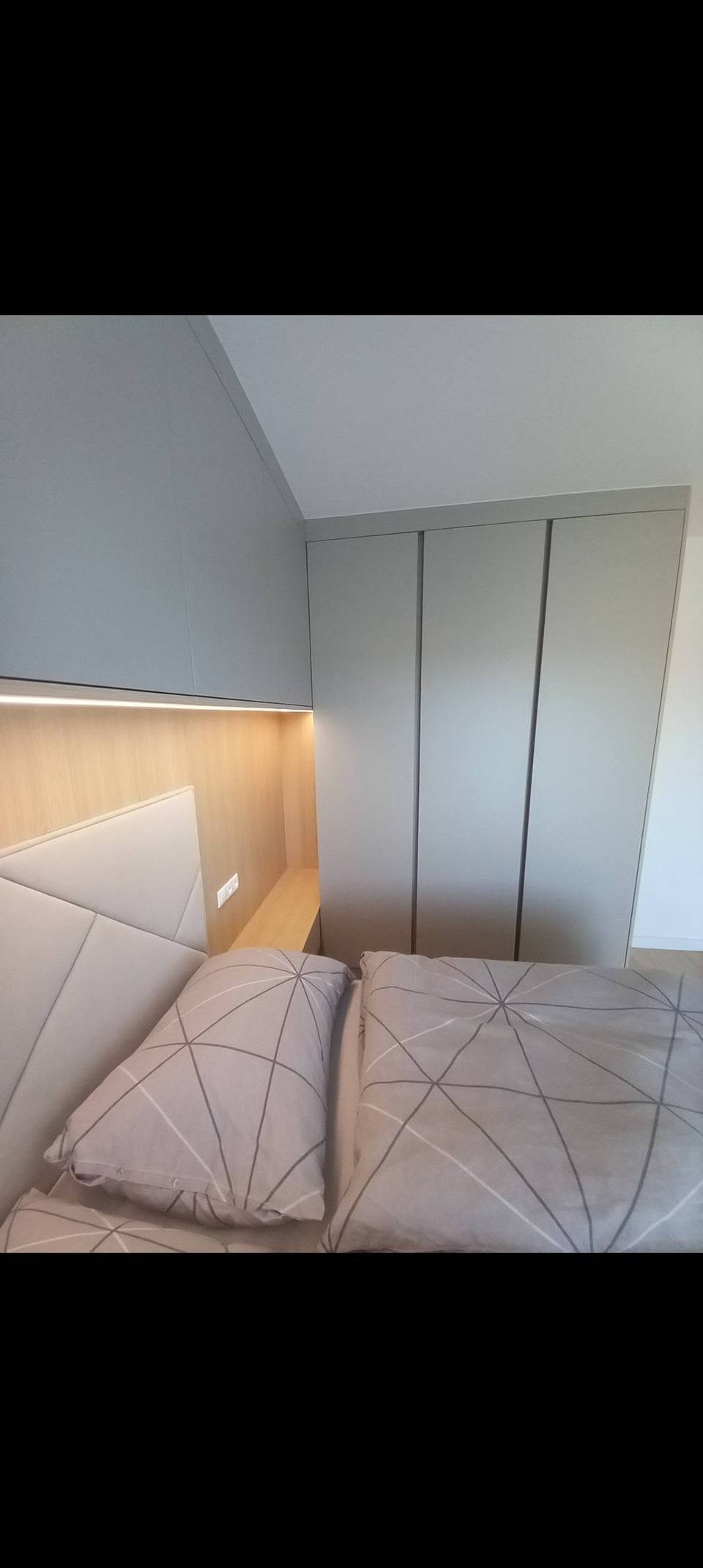 Bett unter der Dachschräge neben grauem, grifflosem Kasten