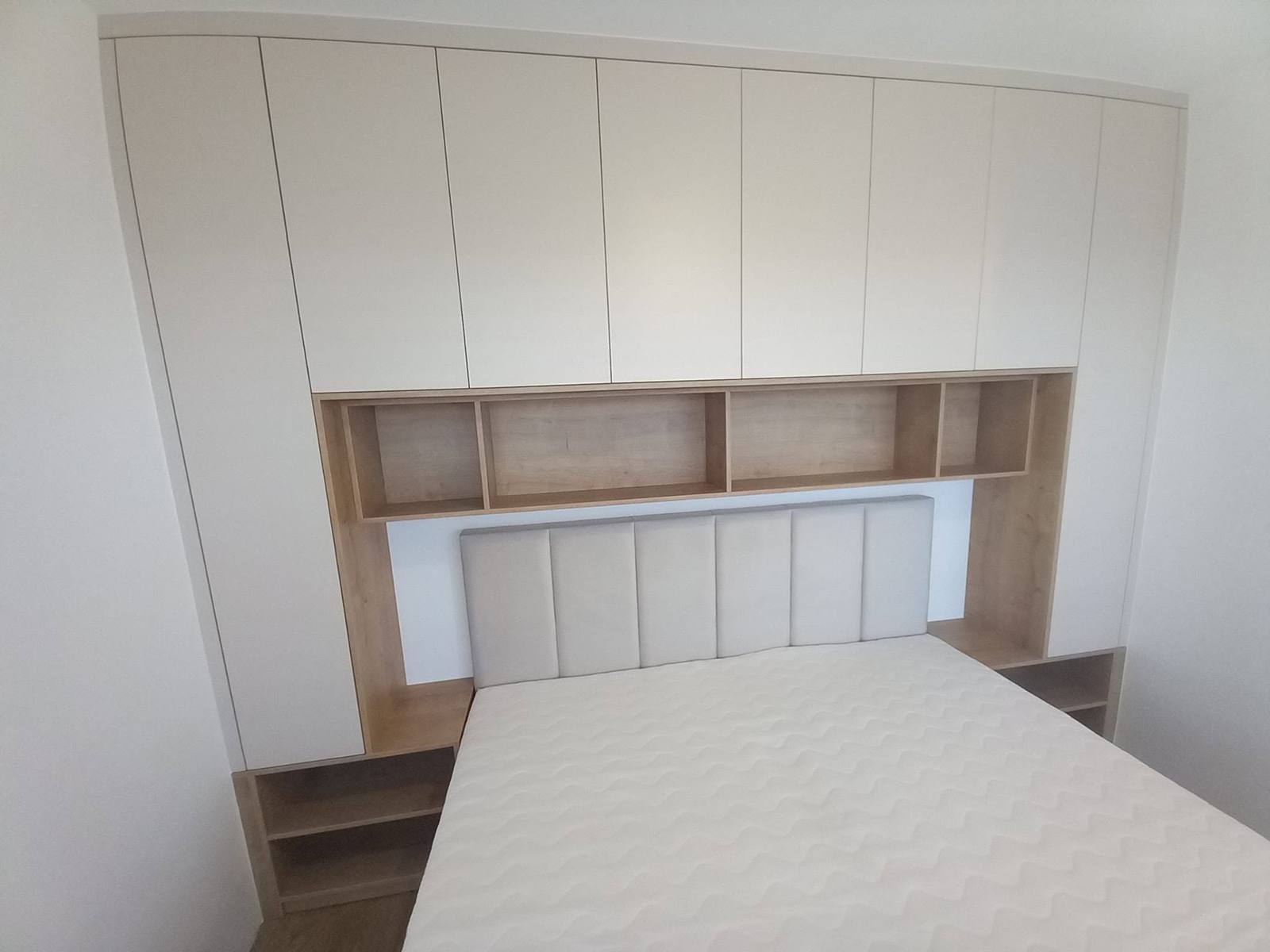 Bett mit Polsterkopfteil, eingebaut in eine helle Kastenwand