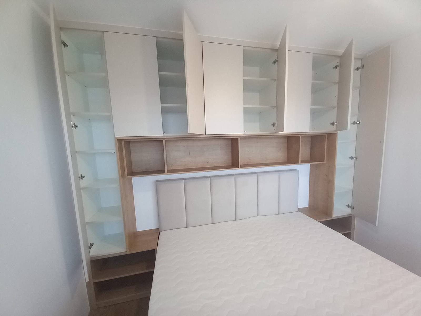 Geöffnete Seitenkästen mit Glasfachböden rund um das Bett