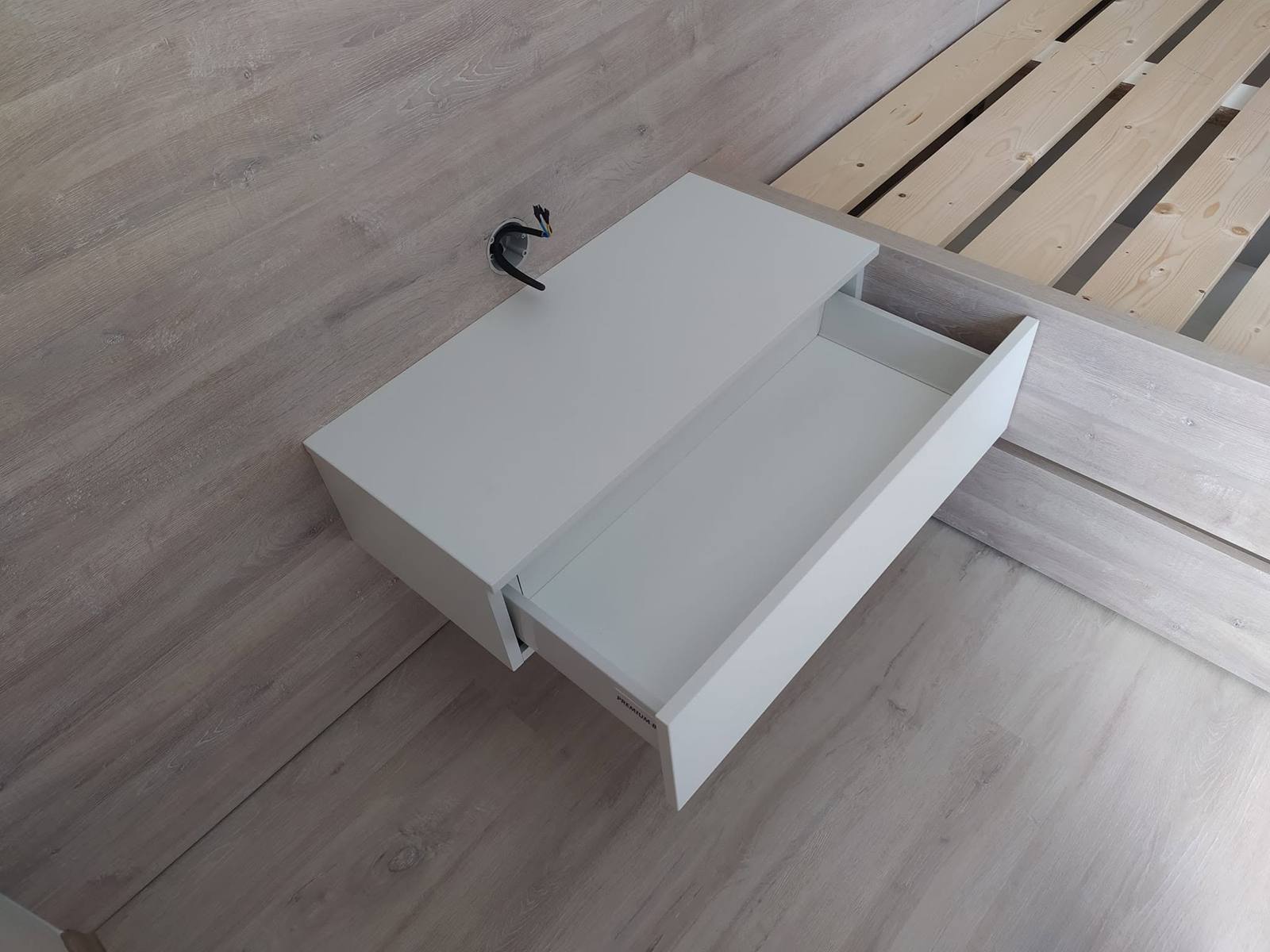 Weißes hängendes Nachtkästchen mit geöffneter Lade am Bett