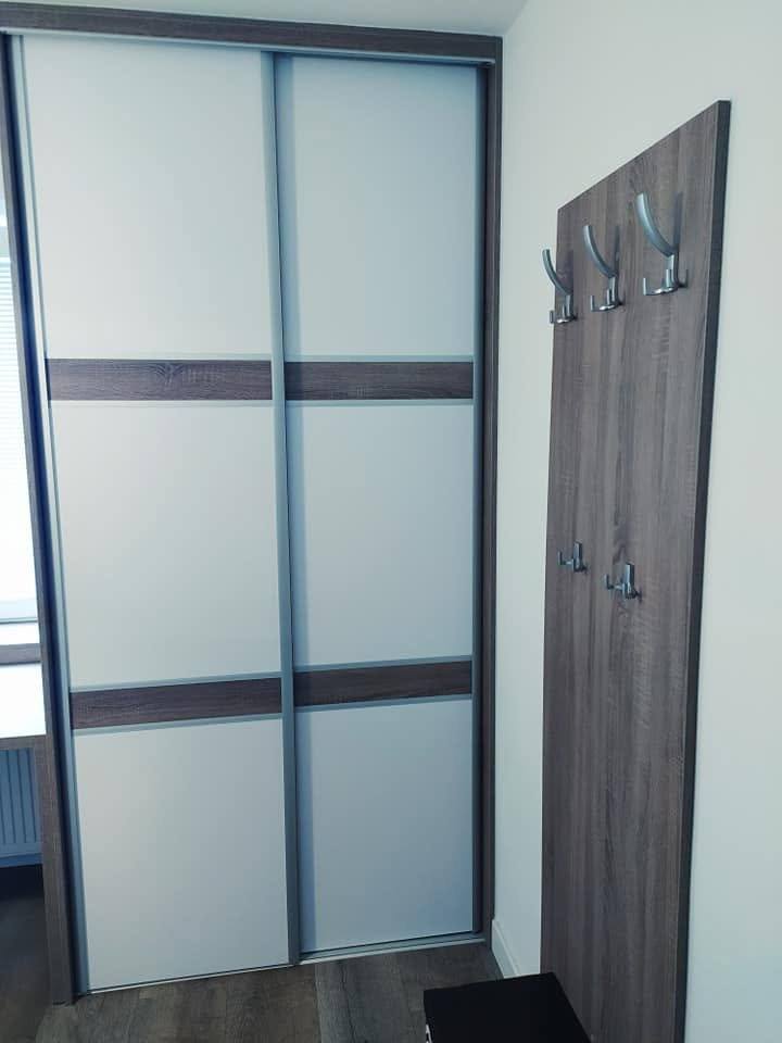 Schiebetürenkasten mit dunklem Rahmen neben einer hohen Garderobensäule mit Haken.