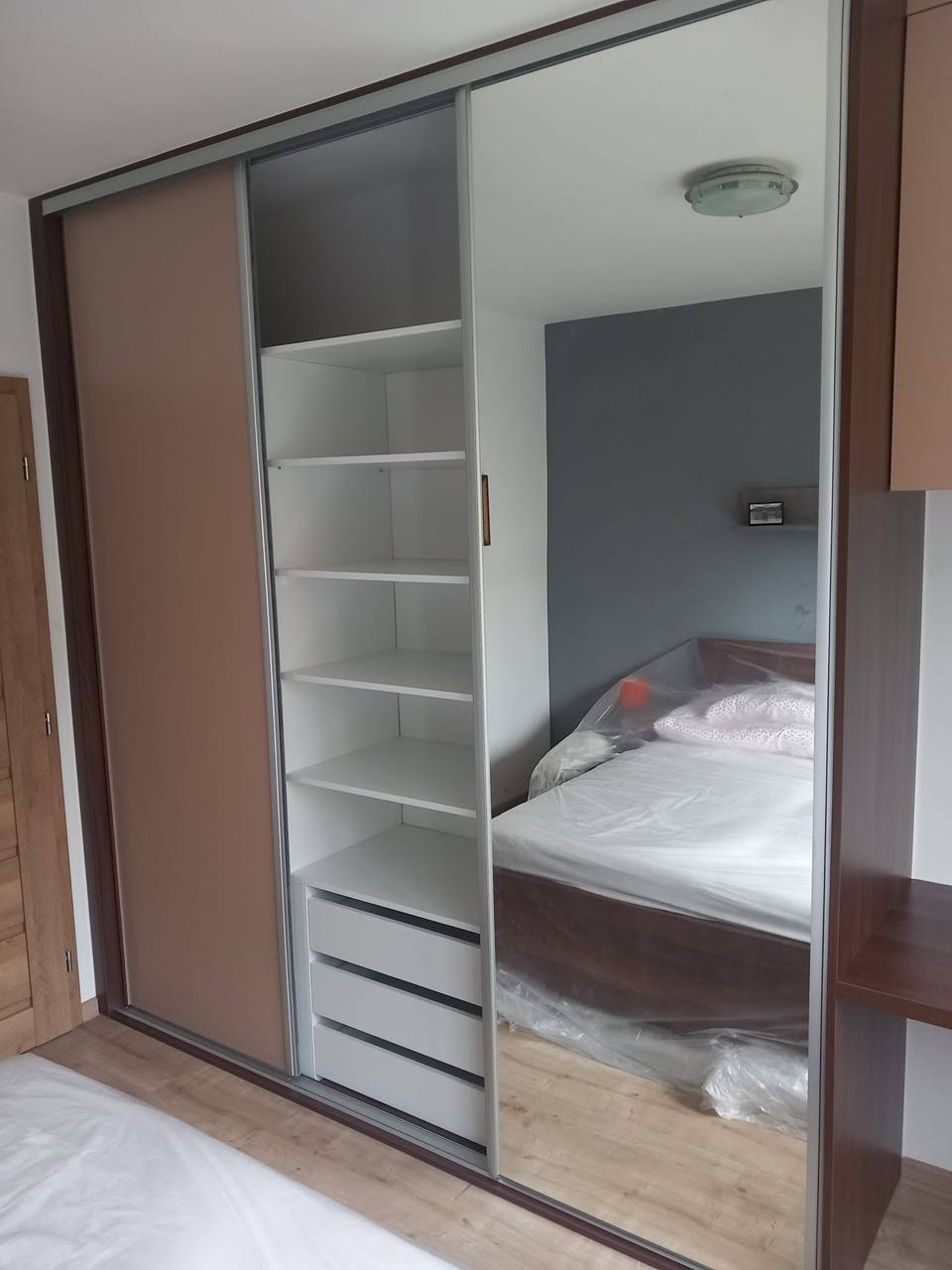 Offener Schwebetürenkasten mit weißen Borden und Spiegel am Bett