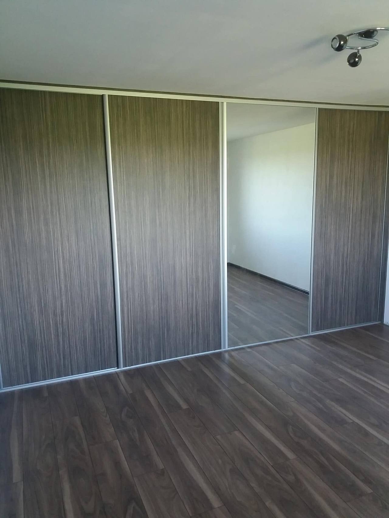 Posuvná skriňa v sivohnedom dekore so zrkadlom v prázdnej izbe