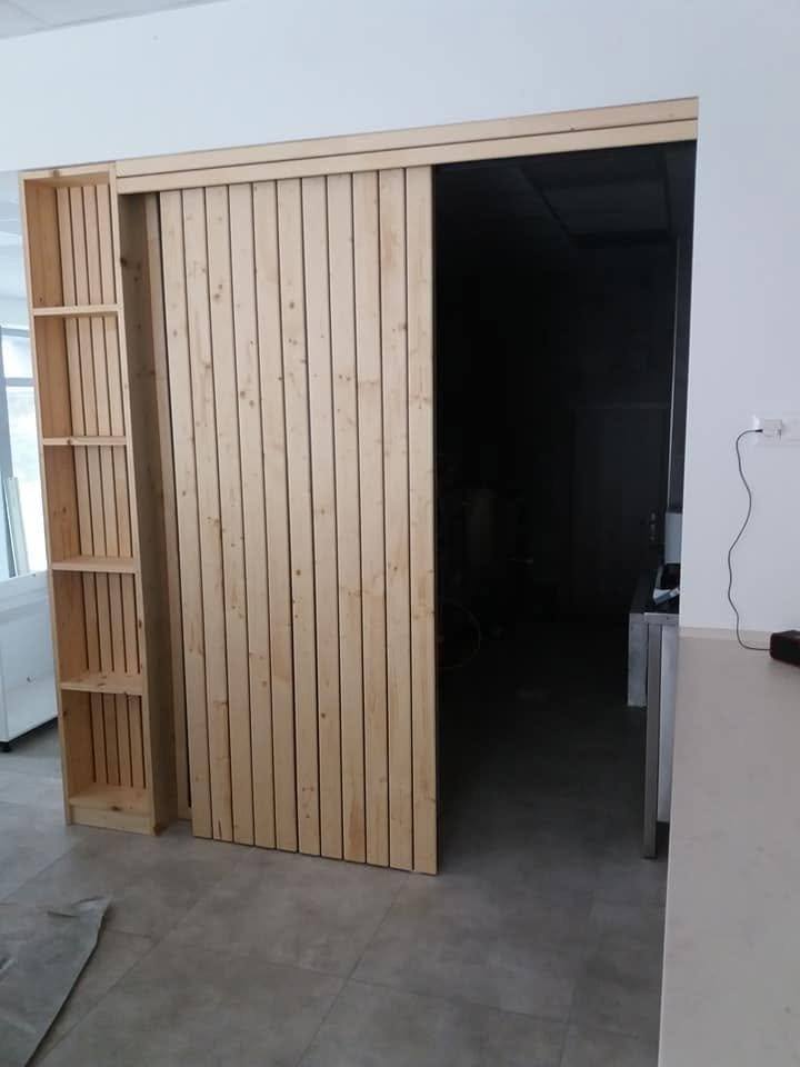Zur Seite geschobene Fichtentür gibt die Öffnung neben dem Regal frei