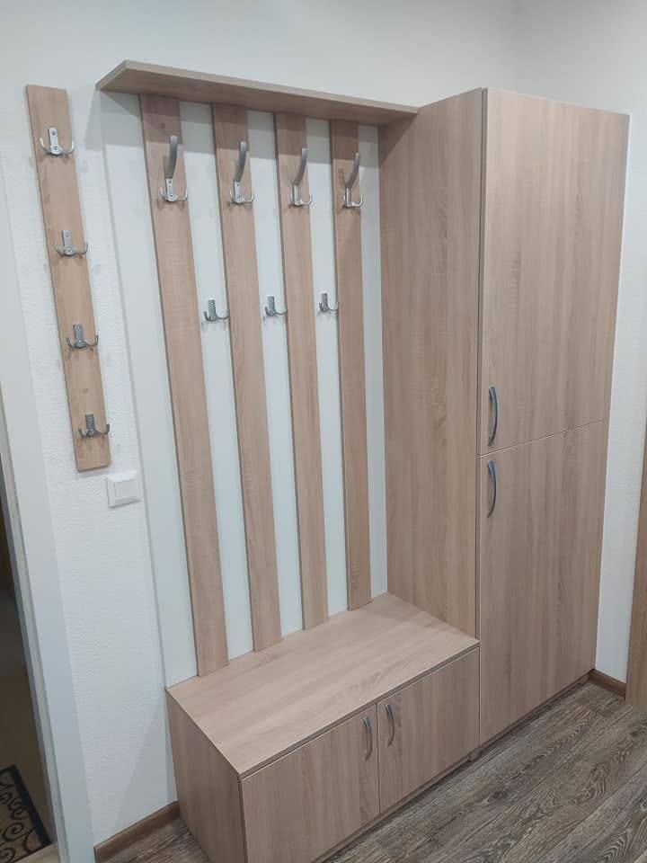 Hoher cremefarbener Kasten neben einem Garderobenpaneel in Eichendekor mit Haken.