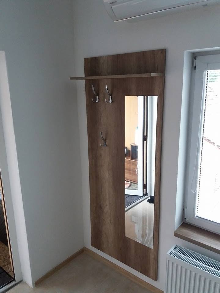Hoher Spiegel neben einer Kleiderstange mit Haken in Eichendekor beim Fenster.