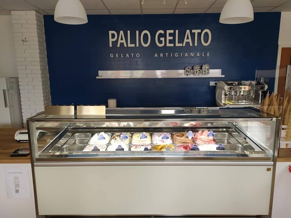 Gelateria-Theke mit Kühlvitrine vor dunkelblauer Wand mit Logo