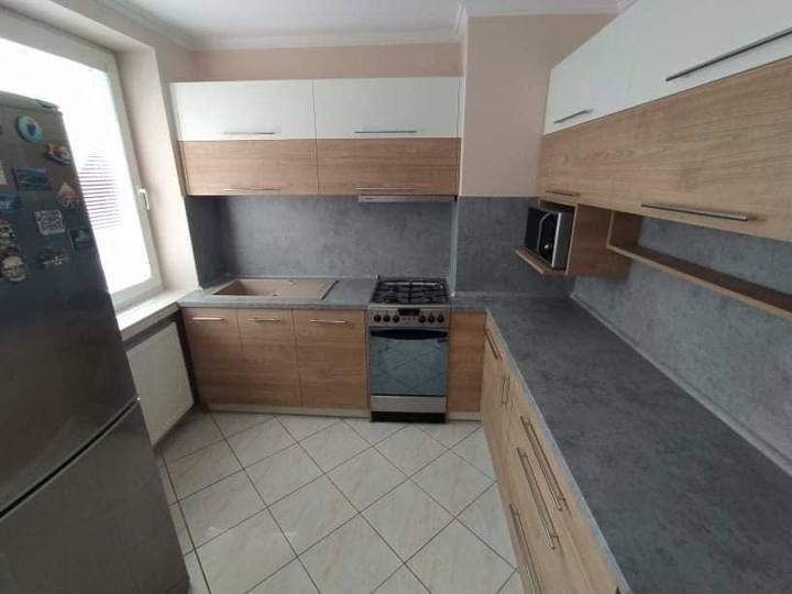 Küchenzeile in Holz und Weiß mit dunkler Arbeitsplatte am Fenster.