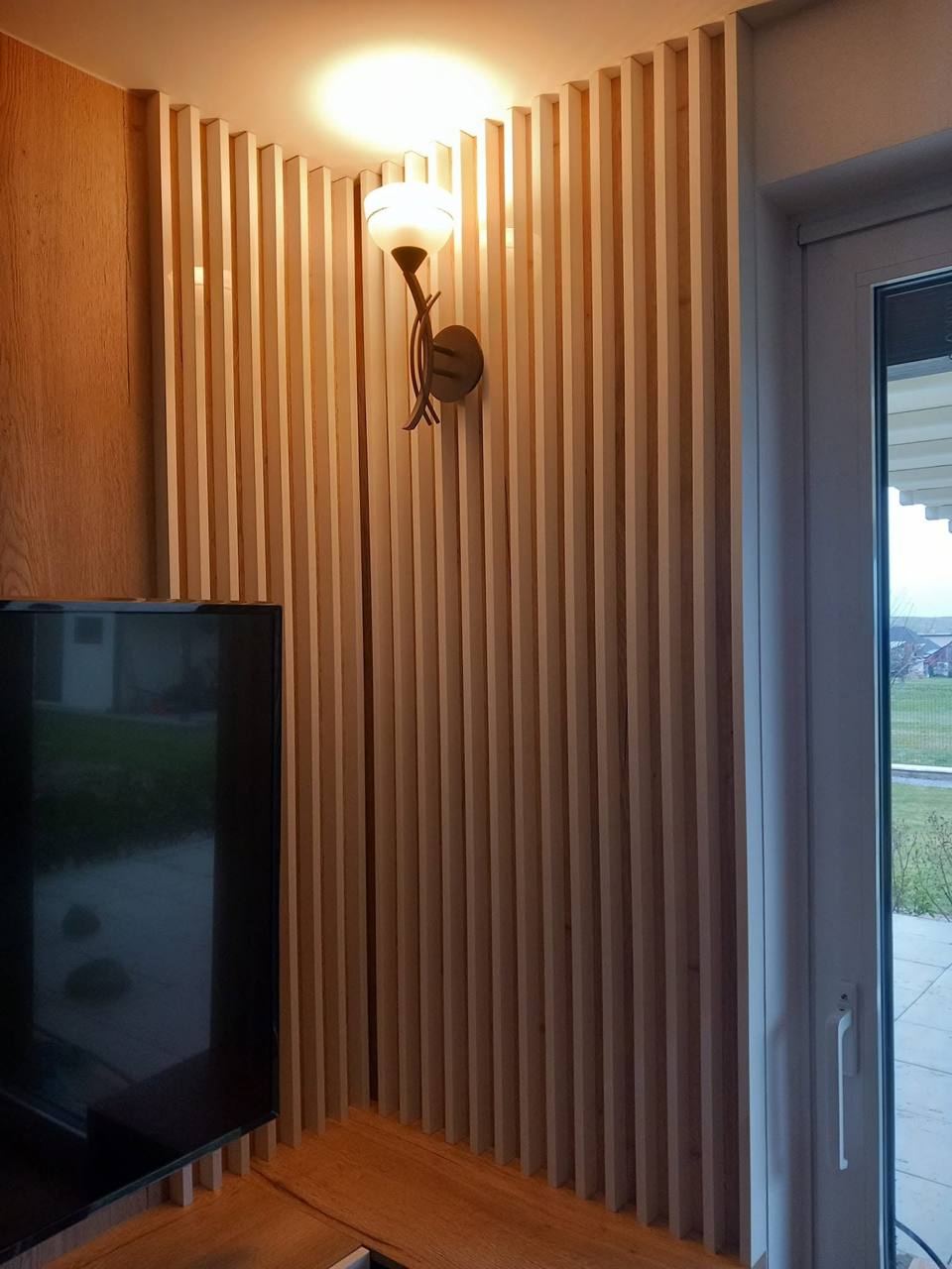 Eckwand mit Holzlamellen, Fernseher und Wandleuchte