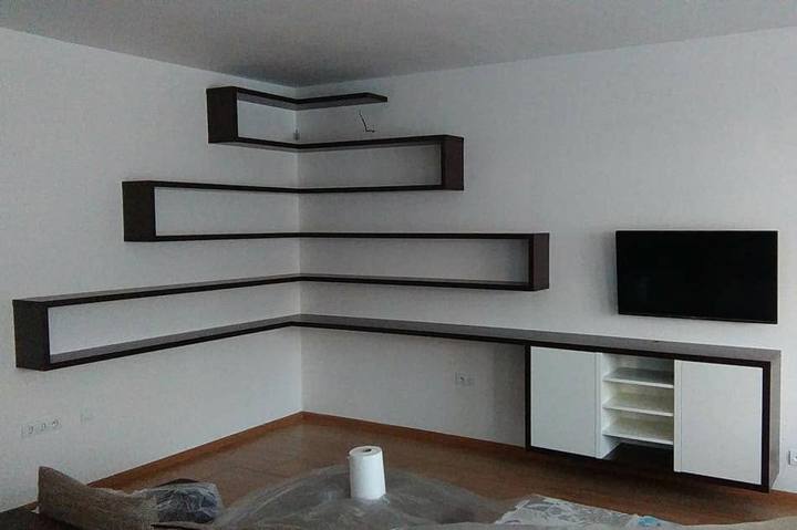 Abgewinkelte Regale auf drei Ebenen über dem TV-Kästchen