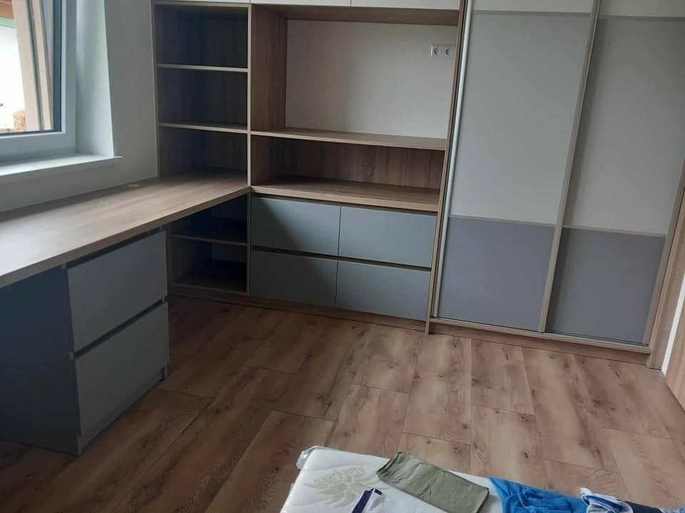 Rohový písací stôl so sivými zásuvkami a policami v izbe