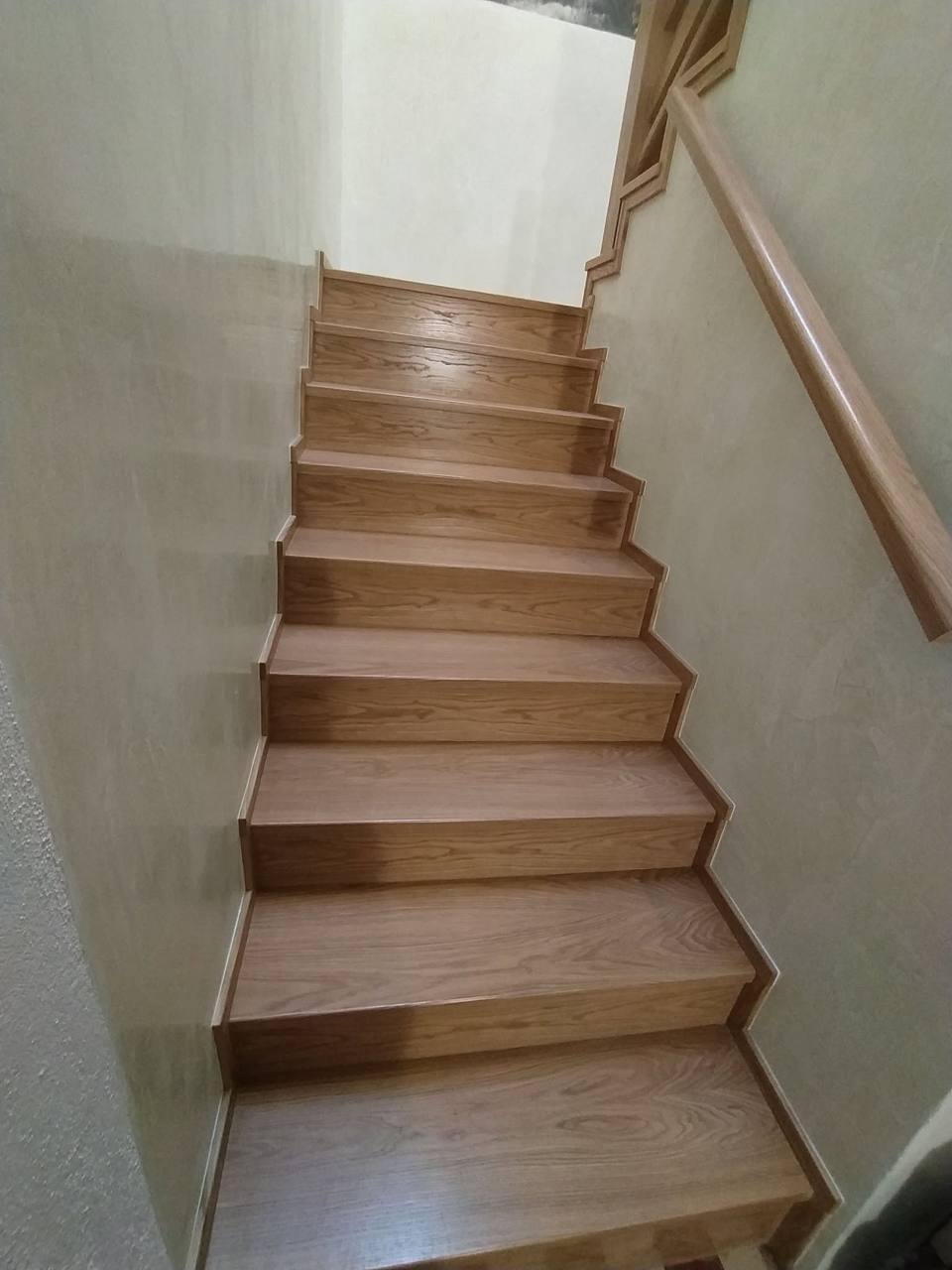 Gerade Eichenstiege mit Holzhandlauf an der cremefarbenen Wand