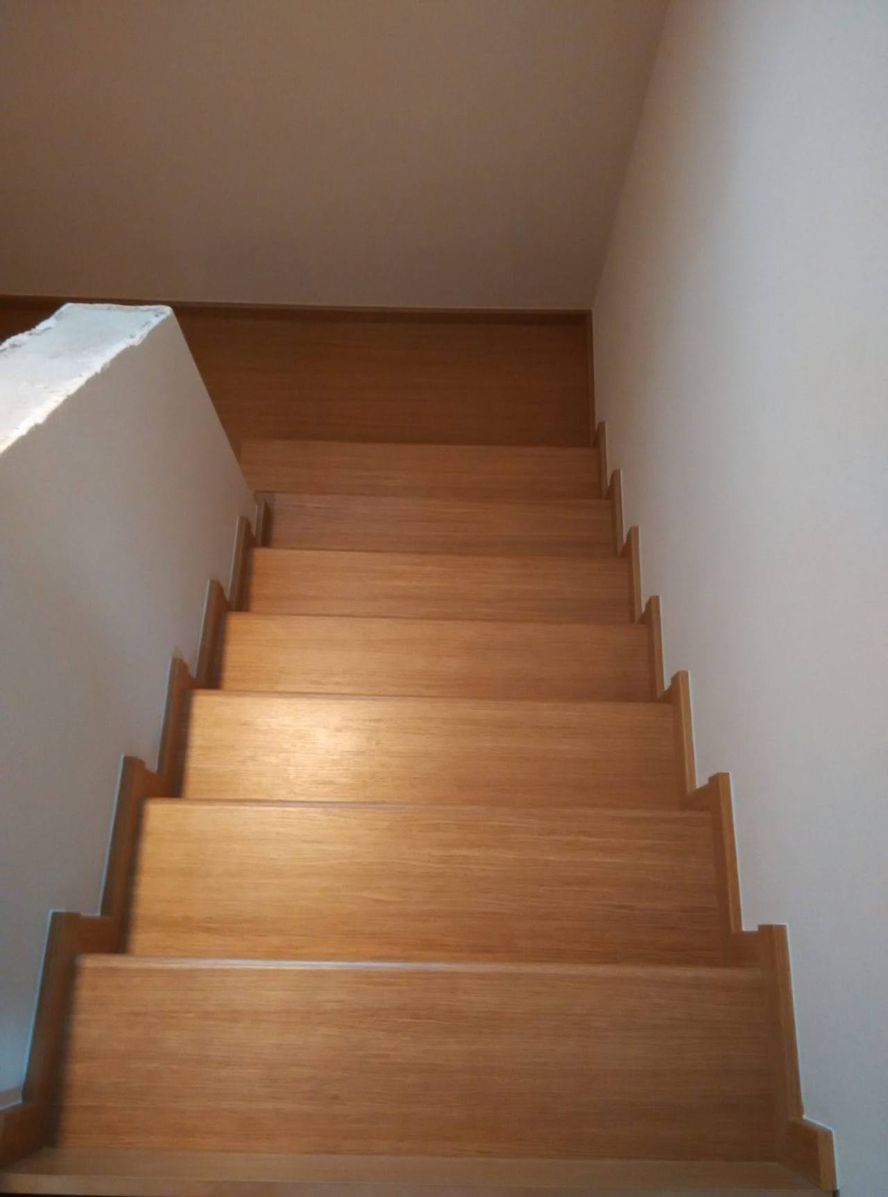 Gerade Eichenstiege von oben zwischen weißen Wänden mit Dachfenster