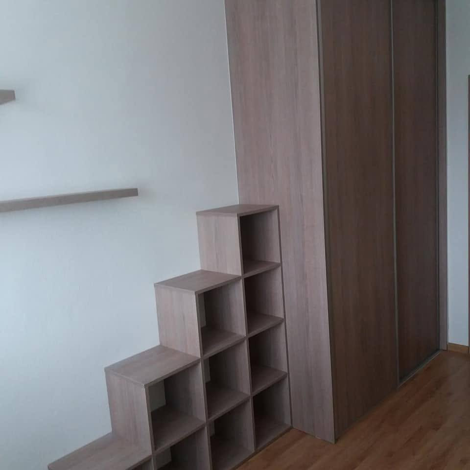 Schodíkový regál v sivohnedom dekore vedľa vysokej skrine