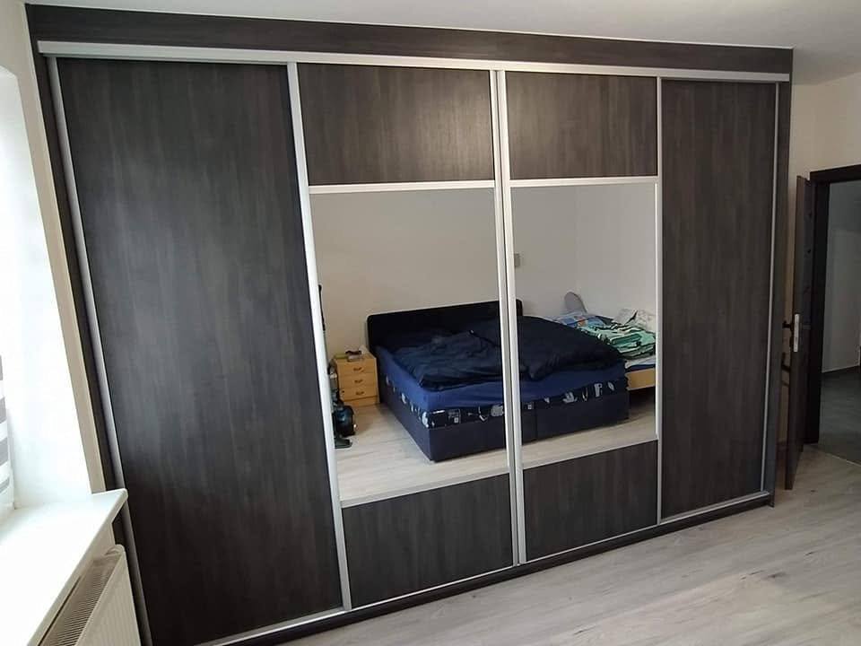Viertüriger dunkler Kasten mit Spiegeln, in denen sich das Bett spiegelt