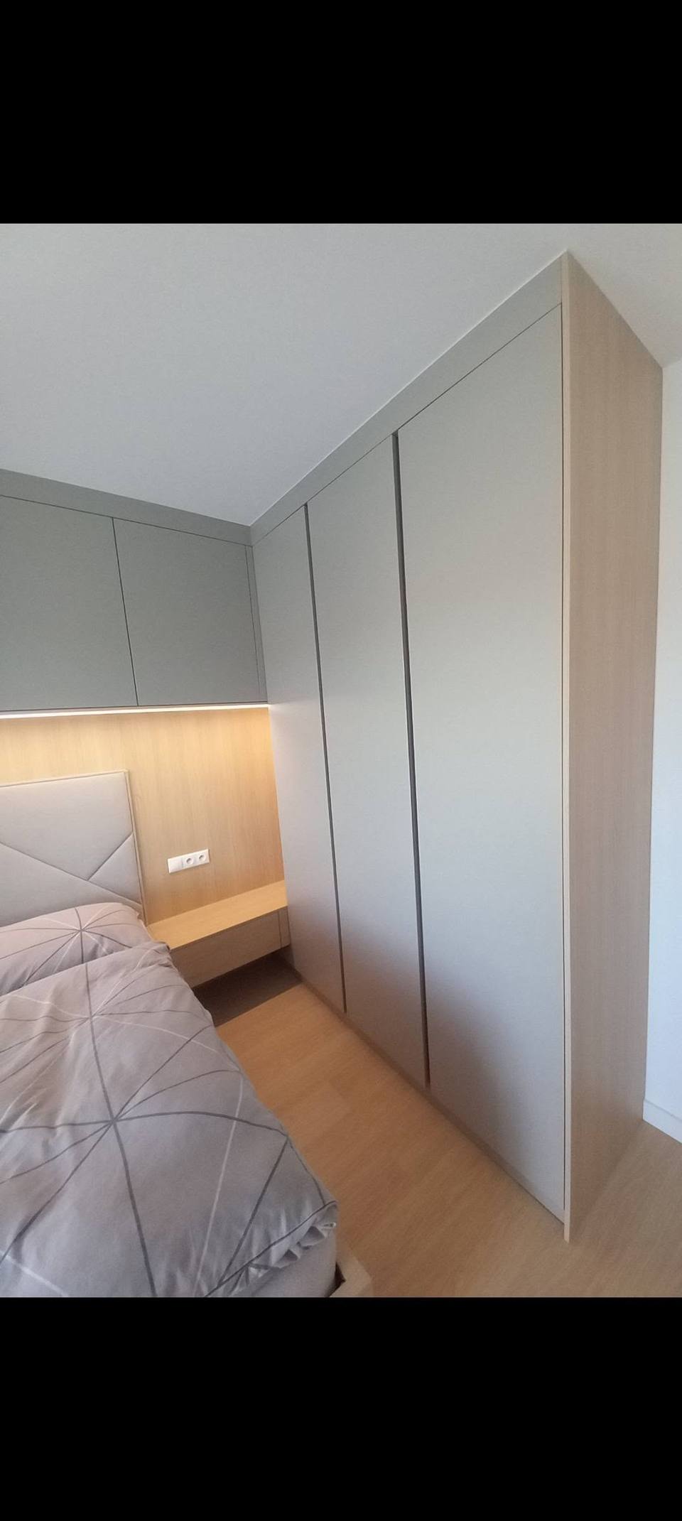 Hoher hellgrauer Kasten beim Bett mit beleuchteter Eichenverkleidung