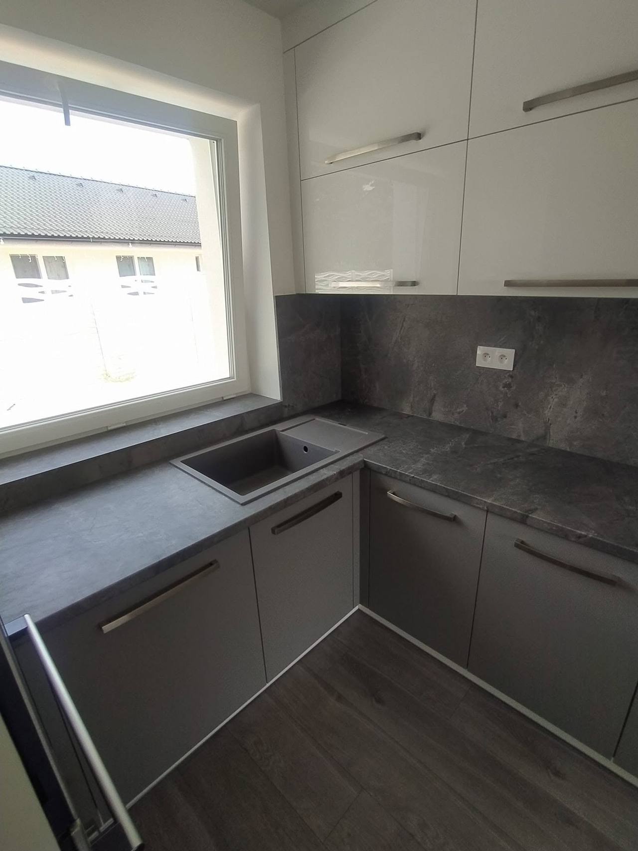 Spüle unter dem Fenster in dunkler Platte mit grauen Kästen