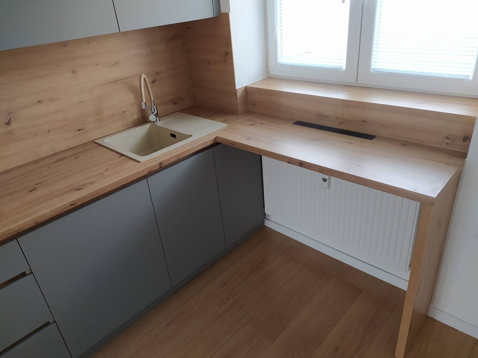 Graue Unterschränke, helle Abwasch und Eichenplatte bis zum Fenster