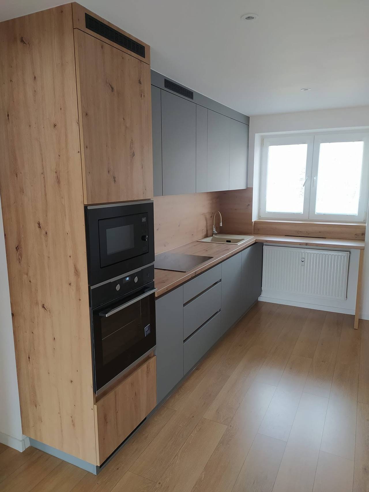 Graue Küche mit hohem Eichendekor-Schrank am Fenster