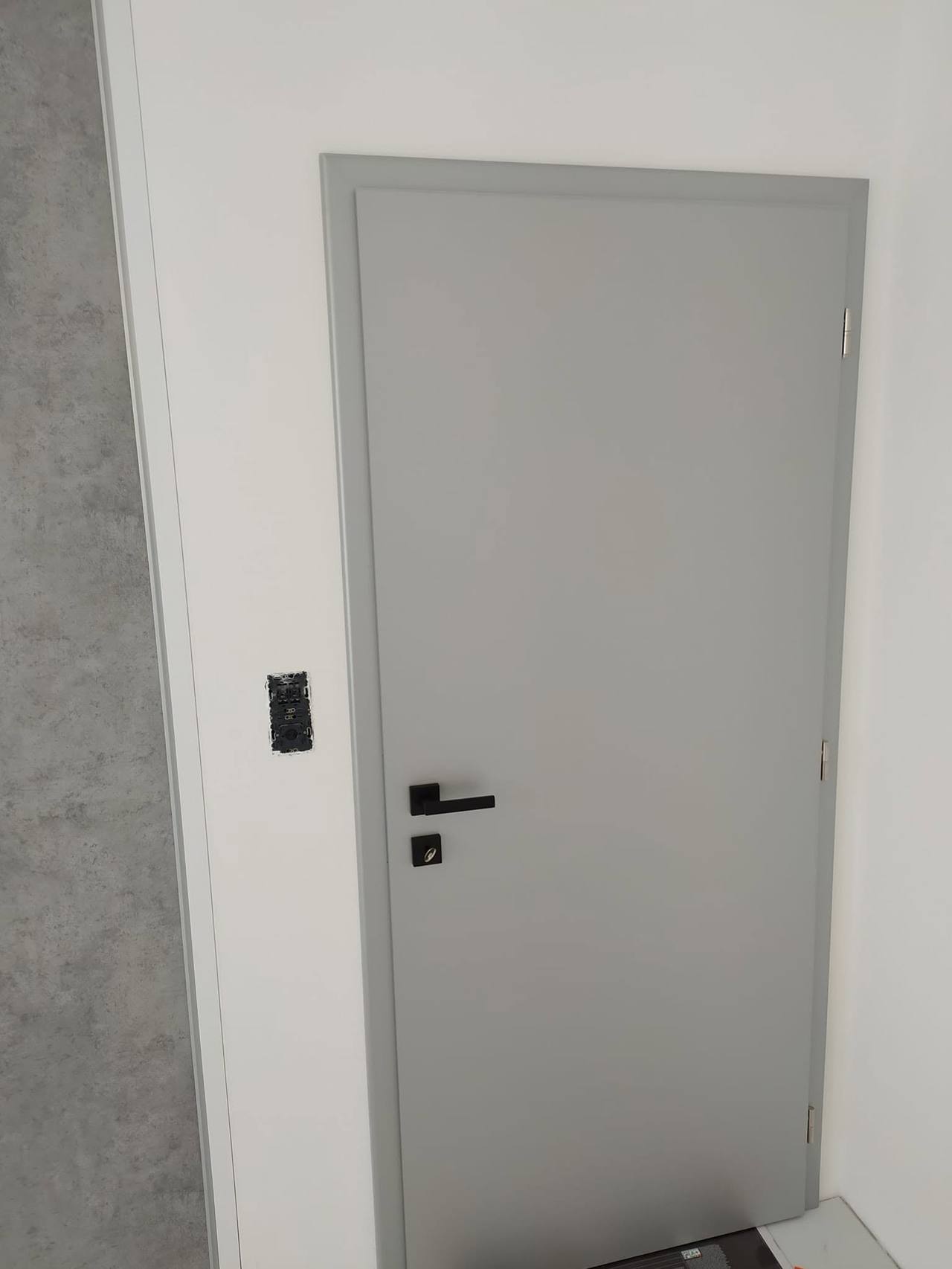 Graue Innentür mit glatter Fläche und schwarzem Griff.