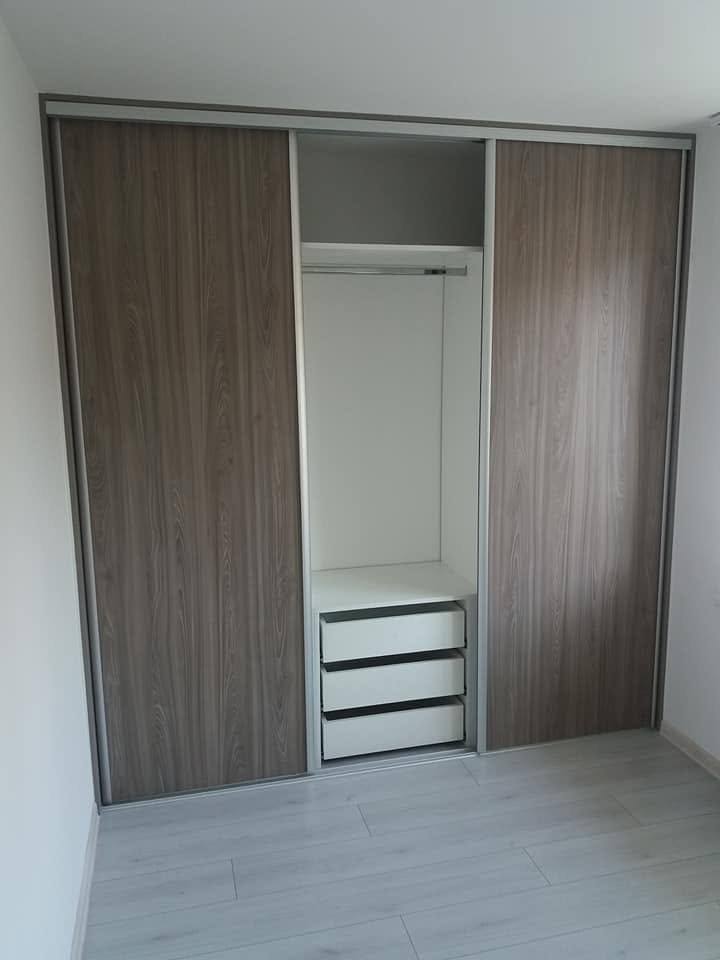 Schiebetürkasten in graubraunem Dekor mit offenem Kleiderbereich und Laden.