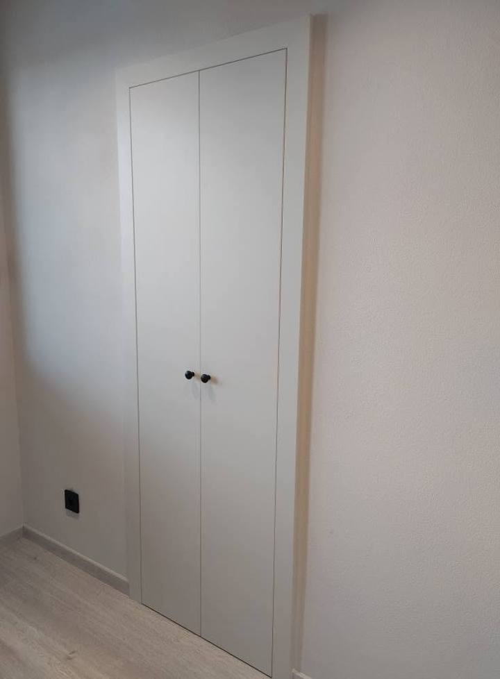 Zapustená biela úložná skriňa s čiernymi gombíkmi v stene