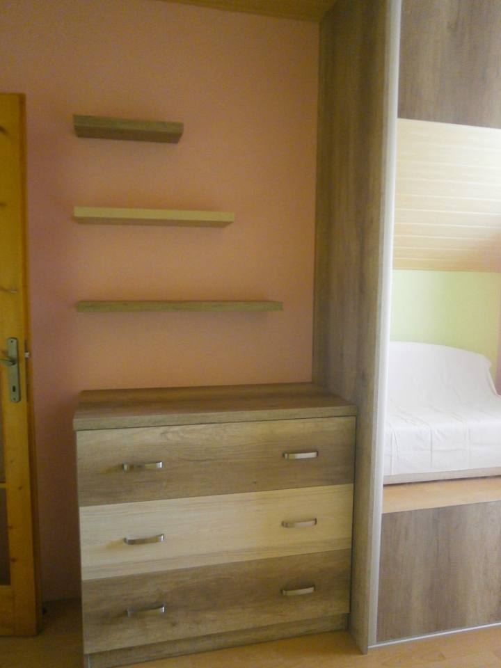 Kommode mit Laden und Wandregalen beim Bett