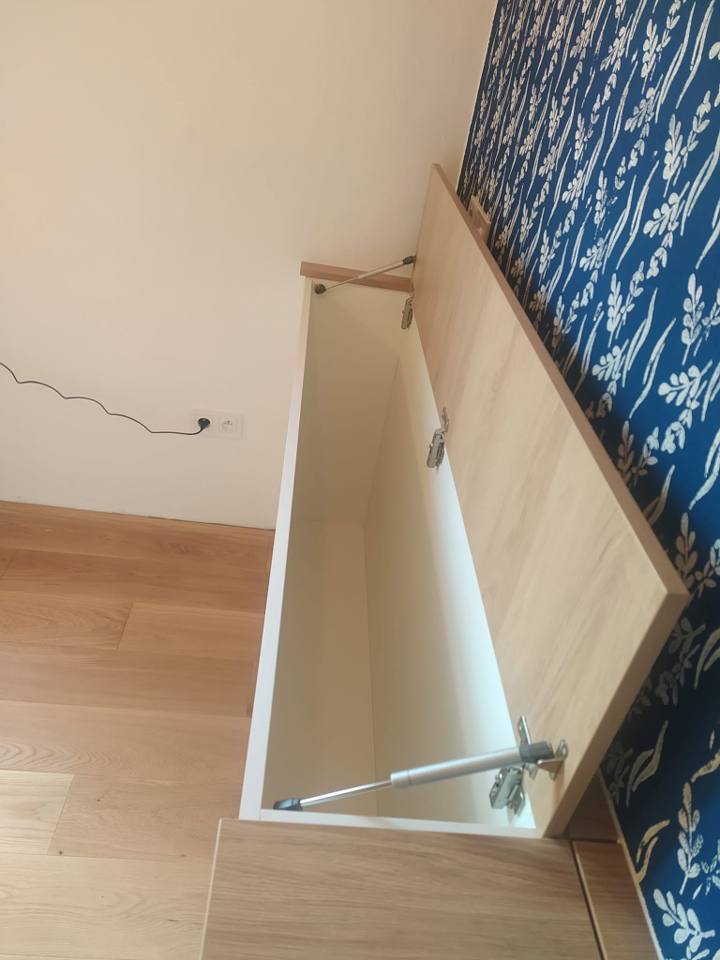 Offener Bett-Stauraumkasten an Wand mit blauer Tapete