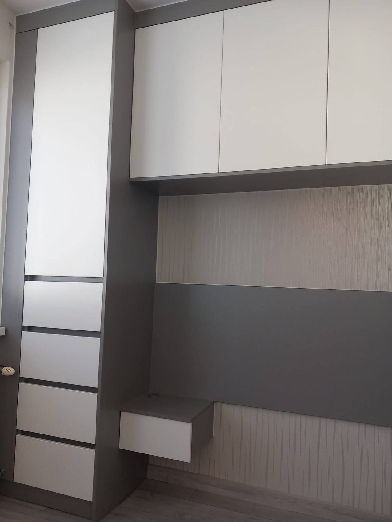 Weiße Ladensäule und graue Wandverkleidung hinter dem Bett