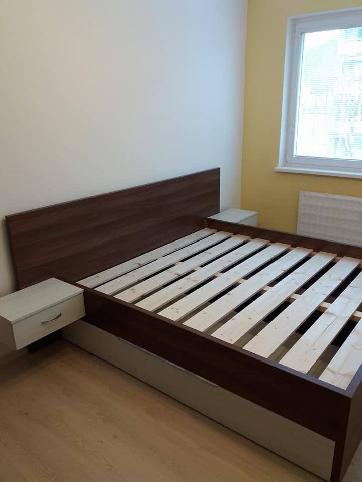 Bett und Nachtkästchen in Nussbaumoptik vor gelber Wand