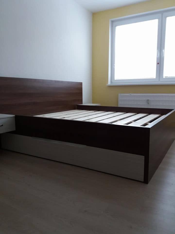 Bett in dunkler Optik mit Nachtkästchen am Fenster