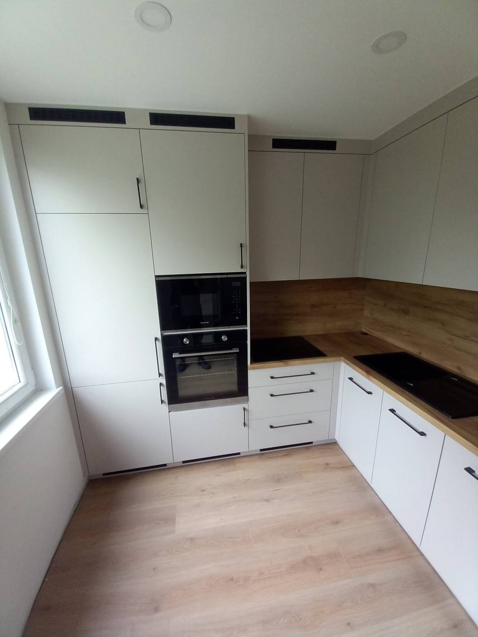 Küche in Kaschmirton mit schwarzen Griffen und Eichenspiegel am Fenster.