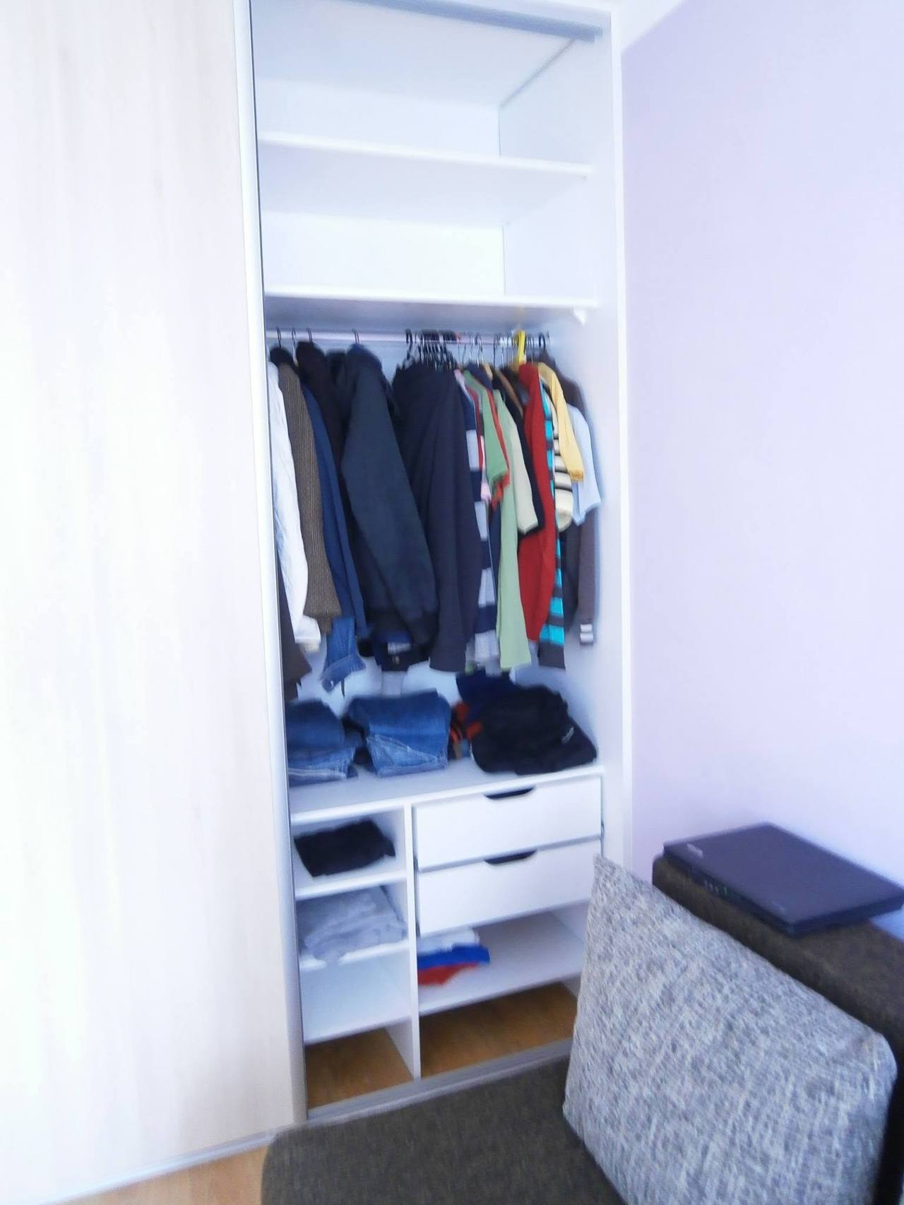Geöffnete Tür zeigt Kleidung auf der Stange und weiße Laden