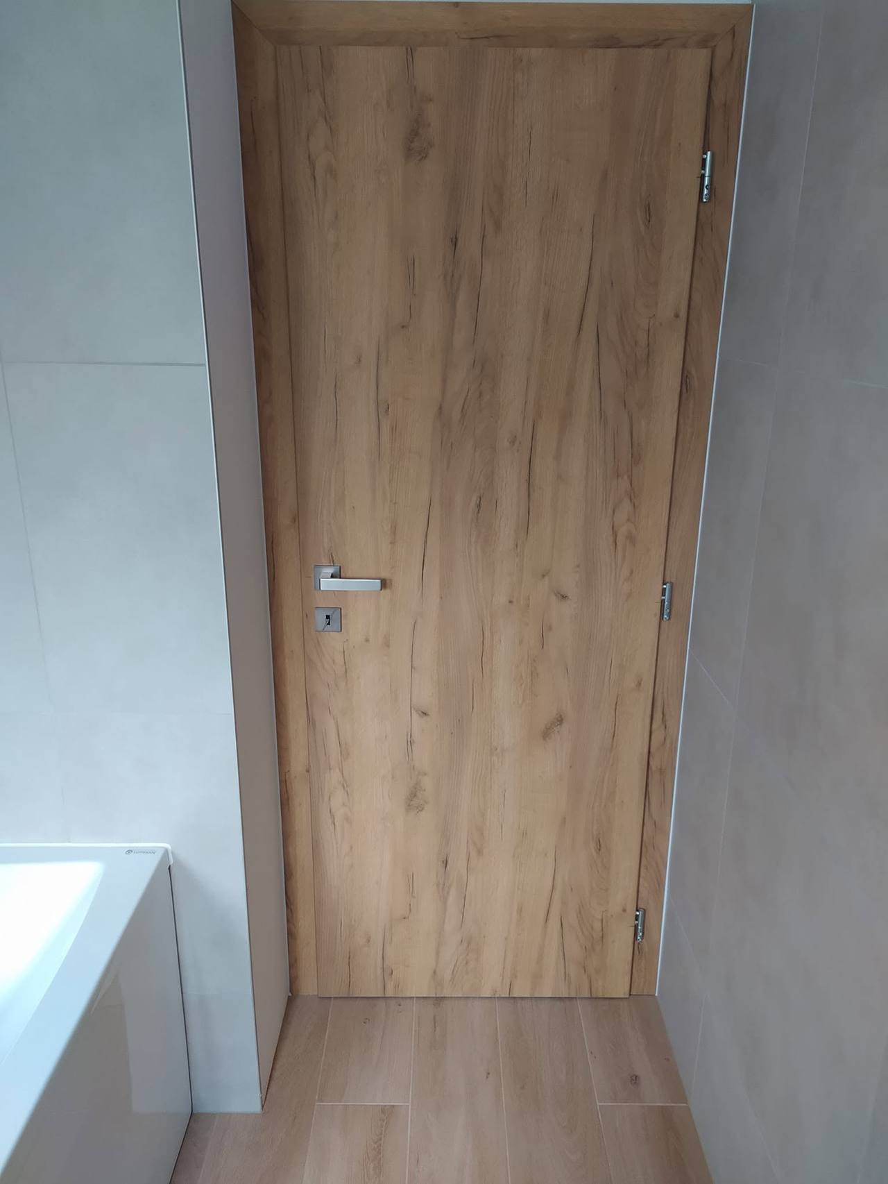 Svetlé dubové dvere pri vani so striebornou kľučkou