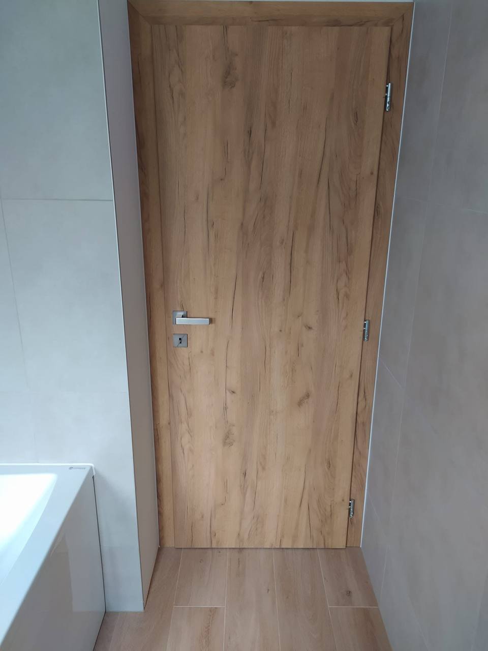 Helle Eichentür bei der Badewanne mit silberner Klinke