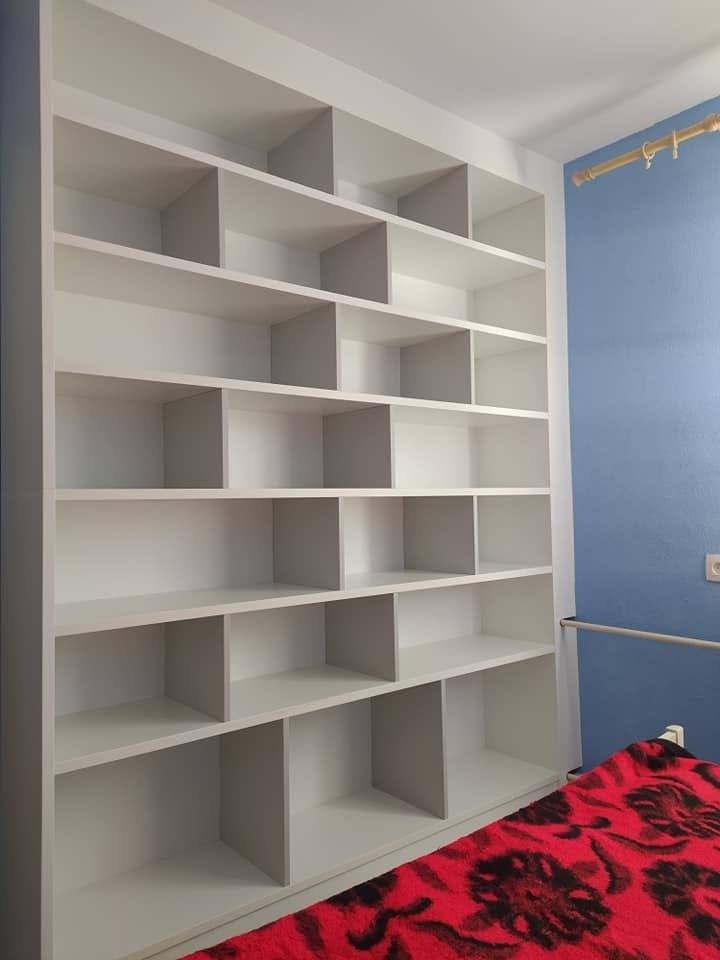 Hohes hellgraues Regal mit versetzten Fächern neben blauer Wand