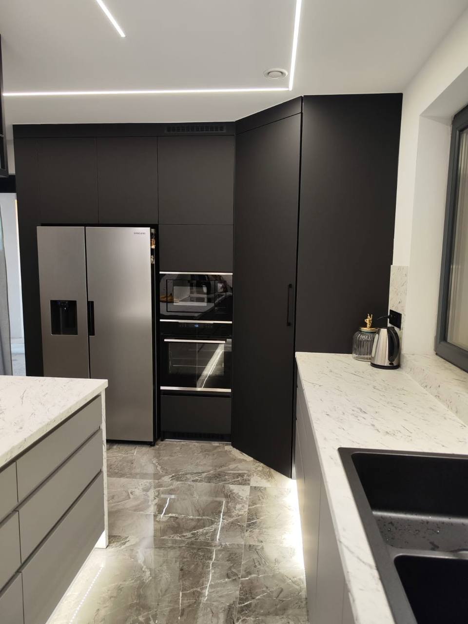Dunkle Eckwand mit Kühlschrank, Backrohr und Platte in Marmoroptik