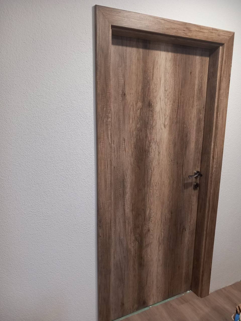 Dunkle Tür in Eichendekor mit Türstock im weißen Vorzimmer