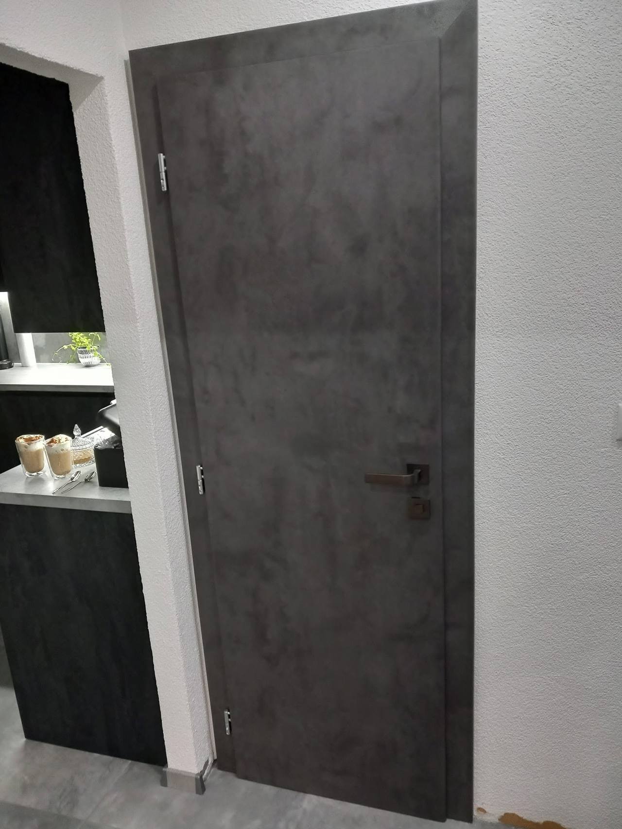Dunkelgraue Tür in Betonoptik neben einem Regal mit Accessoires