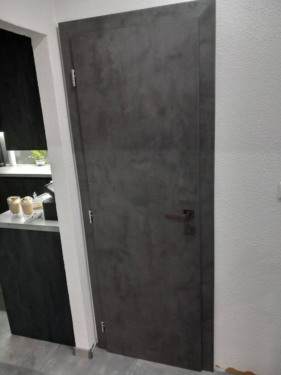Dunkelgraue Tür in Betonoptik neben einem Regal mit Accessoires
