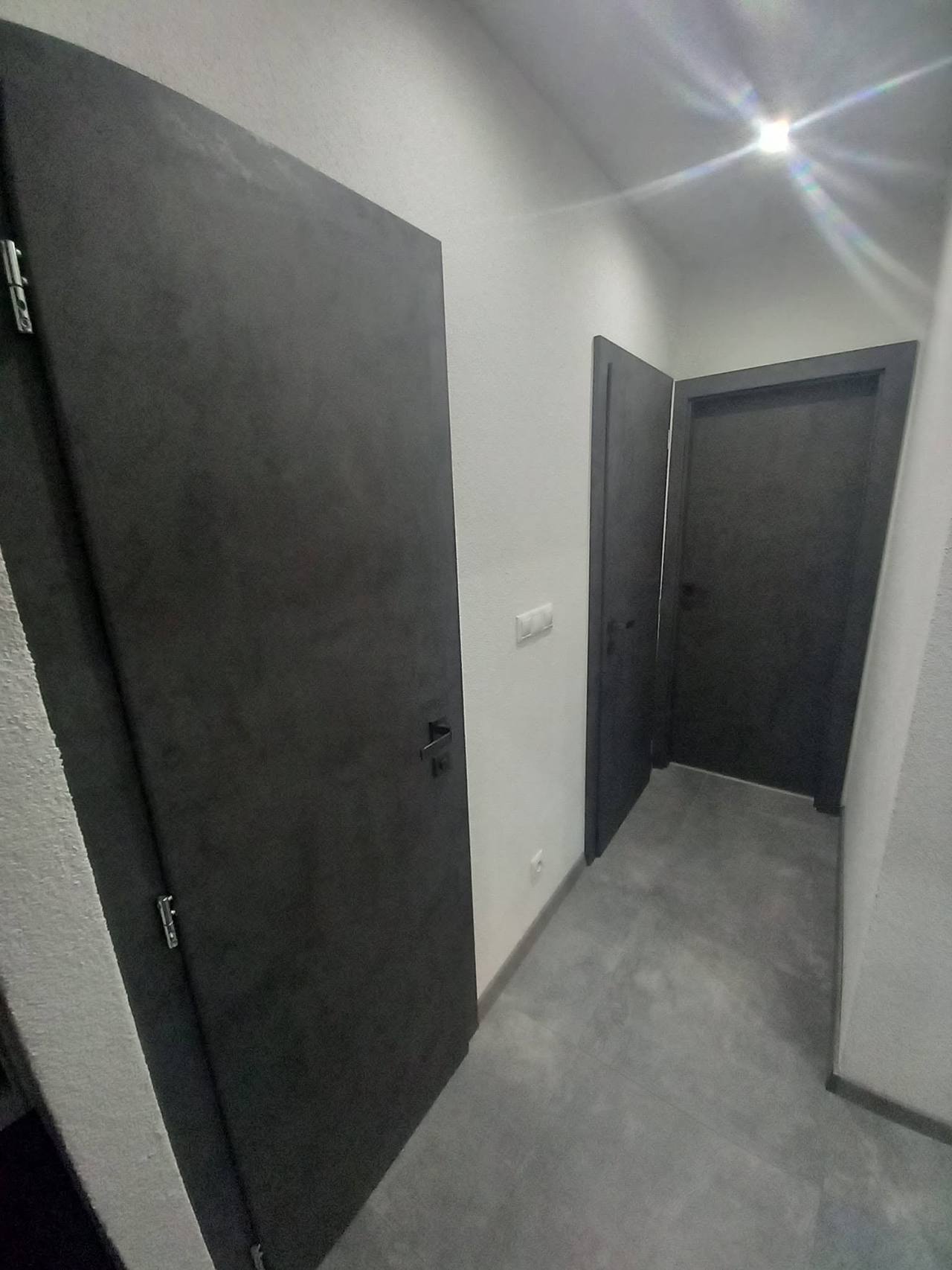 Geöffnete dunkelgraue Tür mit Blick in den Flur mit dunklen Fliesen